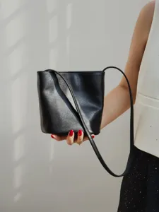 Vue détaillée de sac seau en cuir noir, design bandoulière minimaliste avec sangle fine et texture.