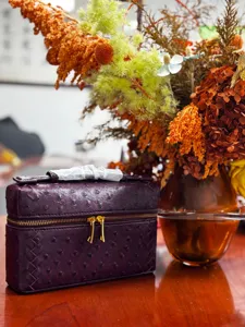 Bolso cosmetico vanity tejido en purpura oscuro con patron de avestruz y cremalleras.