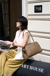 Brown leather shoulder bag with long handles and side buckle detail for women daily use.