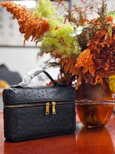 Bolso vanity negro con textura de avestruz, borde trenzado elegante y cremalleras doradas de lujo.