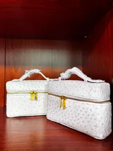 Elegante neceser blanco tipo vanity con diseño trenzado de avestruz y detalles dorados.