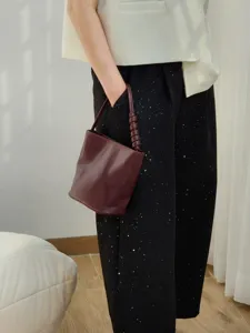 Gros plan du sac seau en cuir bordeaux dote d'une poignee tordue elegante et unique.