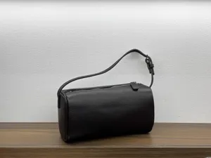 Dark brown cylindrical leather shoulder bag detail shot, minimalist design, smooth zipper.