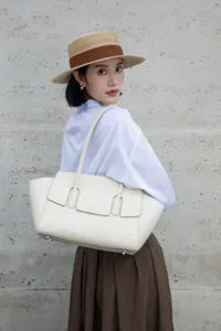 Detailed view of elegant white leather tote bag carried by model against textured wall.