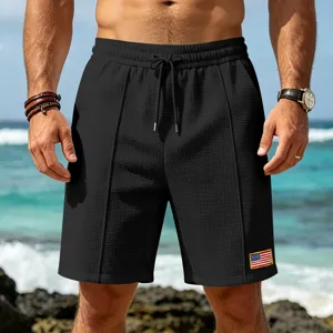 Detail view of men's casual waffle knit beach shorts in black with drawstring and flag patch.