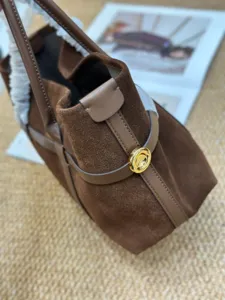 Detalle de primer plano del bolso de ante marrón con cierre metálico dorado y correa.