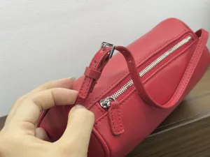 Red leather cylinder bag detail view, showing fine zipper and adjustable strap hardware.