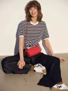 Red leather cylindrical shoulder bag detail shot worn by model with casual outfit and sneakers.