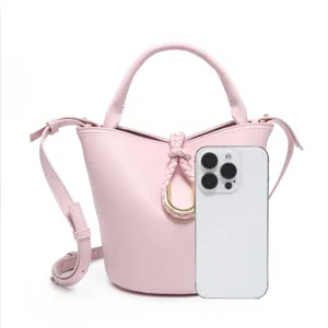 Pink bucket bag detail showing braided ring decoration, handle, and strap against white background.
