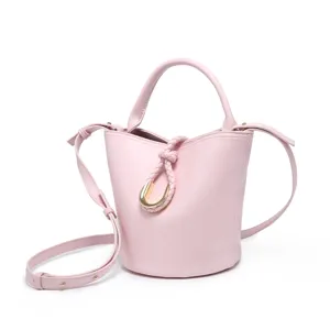 Detailed view of pink bucket bag with braided knot strap and gold U-shaped metal hardware.