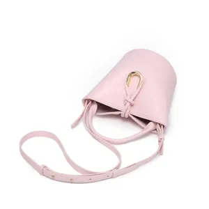 Pink bucket bag with unique horseshoe ring buckle and braided handle detail. Stylish crossbody.