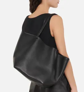 Detail view of a minimalist black leather tote bag worn on shoulder, large capacity chic.