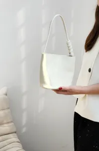 Détail de sac sous les aisselles en cuir blanc, sac seau minimaliste avec poignée nouée.