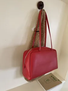 Detail shot of minimalist red leather bowling bag, smooth texture, slim shoulder straps.