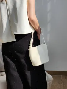 Vue détaillée du sac seau minimaliste en cuir blanc porté élégamment sous le bras.