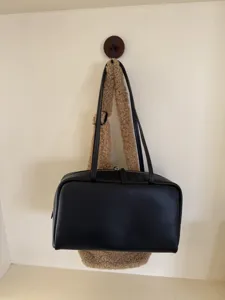 Close-up detail shot of the minimalist black leather shoulder bag hanging on wall hook.