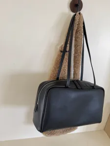 Minimalist black leather bowling bag with dual shoulder straps for women commuting daily.