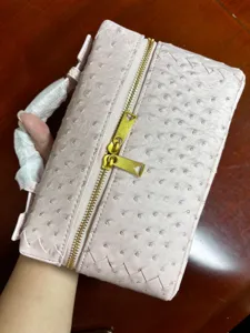 Detalle de bolsa de cosmeticos textura avestruz rosa con bordes tejidos y doble cremallera dorada.