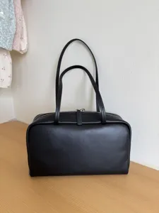 Minimalist black leather bowling bag detail showing smooth texture and dual handles.