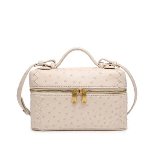 Vista detallada del bolso vanity beige con textura de avestruz y detalles tejidos laterales.