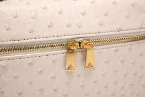 Primer plano detalle del bolso cosmético de cuero avestruz beige con cremalleras doradas.