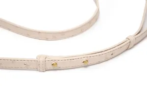 Primer plano de detalle de correa de bolso de cuero avestruz beige con herrajes dorados.
