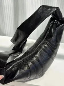 Detail view of black glossy croissant bag with knotted strap and smooth zipper closure.