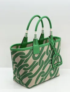 Close-up of green canvas tote bag with leather handles, stirrup charm, and abstract pattern.