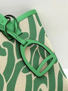 Close-up detail view of green canvas and leather tote bag featuring a distinctive stirrup tag.