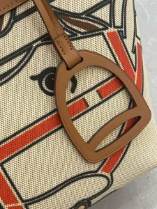 Close-up detail of canvas and leather tote bag featuring equestrian graphic print and stirrup charm.