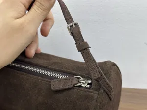 Close-up detail of brown suede cylindrical barrel bag featuring silver metal zipper and hardware.
