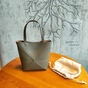 Vue détaillée du sac cabas pliable en cuir vert olive posé sur une table en bois.
