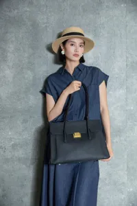 Detail shot of a black genuine leather tote bag held by an Asian model in a studio setting.