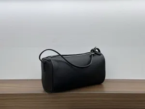 Minimalist black leather cylindrical shoulder bag detail, showing premium texture and zipper.