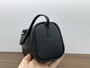 Detailed view of black leather cylinder bag, minimalist design with handle and strap.