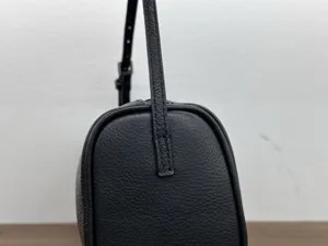 Detailed view of black leather shoulder bag side profile, showing fine grain and strap.