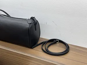 Close-up detail shot of black leather cylindrical barrel bag, showing fine texture and strap.
