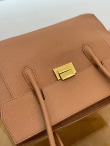 Leather handbag detail view, showing premium cowhide texture and metallic lock hardware.