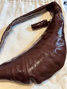 Close-up detail of the glossy brown croissant shoulder bag, showing unique stitched panels and knot.