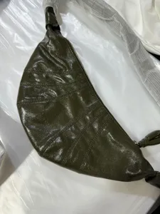 Dark green glossy croissant bag detail shot, showing the unique curved shape and knot handle.