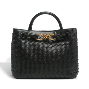 Black woven leather top handle bag with elegant gold metal knot hardware detail for women.