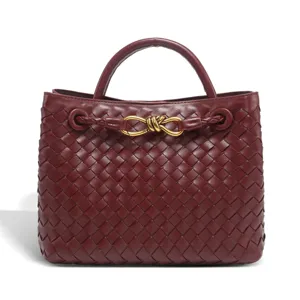 Burgundy woven leather handbag detail with elegant metallic knot closure and fine texture.