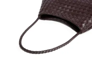 Close-up detail of dark brown woven leather shoulder bag showing intricate braided strap texture.