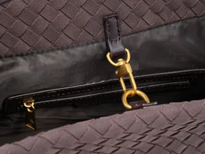 Close-up detail shot of luxury suede woven handbag featuring metallic clasp and zipper pocket.