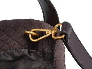 Close-up detail of luxury brown woven leather bag featuring gold hardware and leather strap.