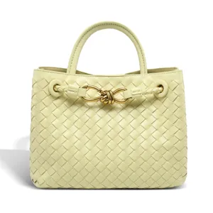 Detailed view of pale yellow woven leather tote bag with elegant metallic knot hardware.
