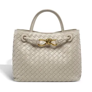 Detail shot of light grey woven leather handbag with elegant metal knot hardware and handle.