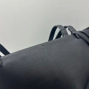 Black leather tote bag close up detail showing pebbled texture and thin handle straps.