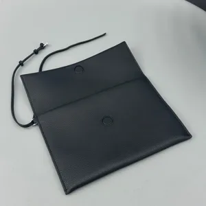 Black leather clutch pouch detail showing fine texture, magnetic snap, and slim strap.