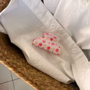Vue détaillée de la jolie pince à cheveux rose à motif de pommes sur chemise blanche.